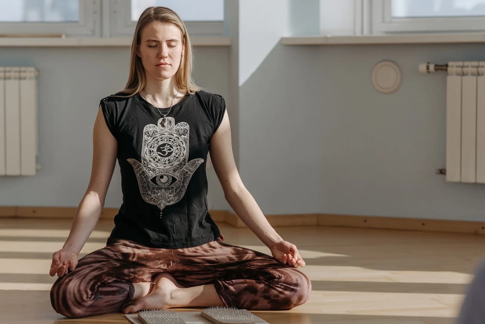 Femme assise en tailleur sur un coussin de méditation, yeux fermés, lumière douce du matin